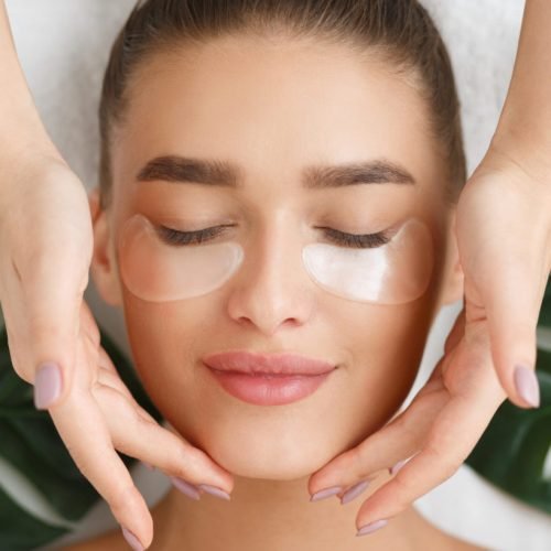 Woman with eye patches having face massage at beauty salon